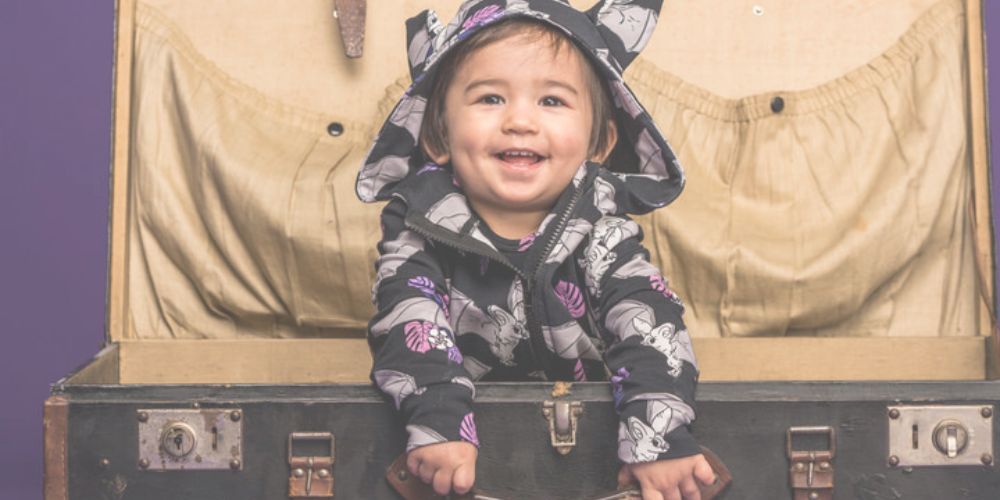 Baby mit Bio Kleidung von Mullido schaut aus dem Wühlkorb Koffer